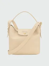 Cartera bucket S Longchamp modelo Le Cadence, confeccionada en cuero granulado color bordó. Presenta solapa frontal con botón a presión metálico dorado y grabado de la marca, asa superior de mano y correa de hombro ajustable y desmontable.