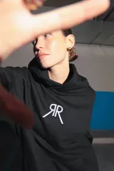 Buzo negro oversize de frisa con capucha amplia, bolsillo canguro, terminaciones de puño y ruedo con rib, y logo bordado en el centro delantero.