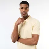 Remera tipo polo de color amarillo claro, con cuello clásico y detalles en blanco en el borde del cuello y las mangas. Presenta cierre frontal de botones y mangas cortas.