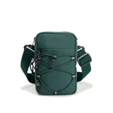 Bandolera de diseño técnico confeccionada en tejido ripstop color verde oscuro. Cuenta con un compartimento principal con cierre, un bolsillo frontal con sistema elástico tipo bungee y una correa de hombro regulable con ganchos desmontables. Presenta logo bordado en la parte superior y detalles reflectantes.