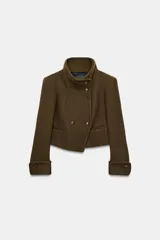 Chaqueta corta de paño color verde militar, con cuello subido, manga larga con puños abotonados y cierre frontal cruzado con botones metálicos. Presenta hombreras y bolsillos de vivo en el delantero.