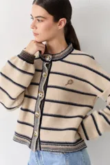 Cardigan rojo de punto amplio con rayas horizontales azul marino, mangas largas abuchonadas y cuello redondo. Cuenta con cierre frontal de botones, detalles en los bordes y un pequeño bordado de raqueta de tenis en el pecho.