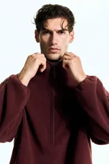 Buzo deportivo de polar color bordó, con cuello alto y cierre frontal parcial. Presenta mangas largas de corte caído y bolsillos laterales integrados en la costura.