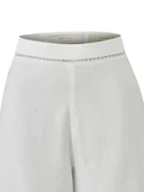 Pantalón de lino orgánico y viscosa, de color blanco y corte recto con tiro alto. Presenta detalles de calados sutiles en la cintura y en los dobladillos.