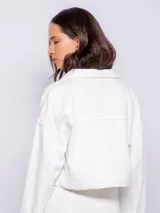 Campera corta de jean color blanco, con cuello camisero, botones metálicos plateados en el frente y puños, y bolsillos delanteros con solapa.