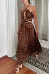 Vestido largo color marrón con estampado de lunares blancos. El top tiene escote halter, detalle de mostacillas y aberturas en el abdomen, con espalda elastizada. La falda es holgada y con elástico en la cintura.