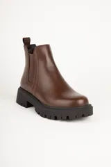 Bota estilo Chelsea de caña baja confeccionada en cuero sintético, con punta redonda, paneles elásticos laterales y suela track dentada de plataforma.