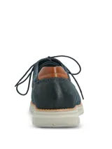 Zapato de estilo casual tipo derby, confeccionado en cuero azul marino con acabado gamuzado. Presenta detalles de costuras decorativas y perforaciones tipo brogue en los laterales, con un detalle en cuero color suela en el talón. Cuenta con cordones al tono y una suela de EVA flexible en color gris claro con tecnología de amortiguación.