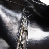 Cartera de hombro tipo hobo confeccionada en cuero negro con acabado brillante. Presenta dos cierres verticales decorativos en el frente, correa ajustable y placa metálica con logo en la parte central.