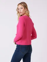 Cardigan de punto color fucsia, con escote a la base, cierre frontal con botones metálicos dorados y terminaciones desflecadas. Presenta bolsillos simulados en la parte delantera y mangas largas.