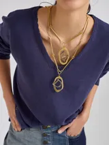 Collar doble de cadena dorada con dos dijes colgantes de formas orgánicas irregulares, cada uno con una letra grabada en su interior.