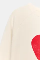 Buzo de algodón color crudo, con cuello redondo, mangas largas ranglán y estampa frontal de un corazón rojo.