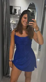 Vestido corto azul eléctrico con brillo, escote drapeado tipo cowl neck y tirantes finos ajustables. La falda es corta y ligeramente acampanada.