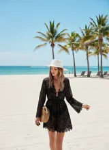 Vestido corto de encaje negro con diseño floral, escote en V profundo y mangas largas acampanadas. Presenta terminaciones con bordes festoneados.