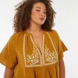 Blusa color mostaza de gasa de algodón con escote en V y bordado floral blanco en el frente.