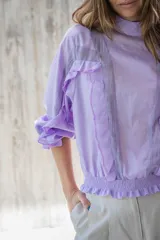 Blusa lila de cuello alto y manga 3/4 con elástico en el bajo. Presenta volados verticales en el frente.