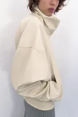 Chaqueta bomber oversize de efecto piel en color crema, con cuello subido, manga larga con hombro caído y cintura con frunces y cinturón ajustable con hebilla metálica. Cuenta con cierre frontal oculto y bolsillos laterales de vivo.