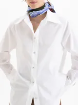 Camisa de poplin color crema, de corte clásico con cuello camisero, mangas largas y cierre frontal con botones dorados de media esfera.