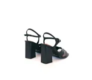 Sandalia de cuero color negro con tiras cruzadas en el frente, pulsera ajustable al tobillo con hebilla dorada y taco ancho alto. La punta es cuadrada y el interior está forrado en cuero.