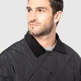 Chaqueta acolchada de diseño romboidal en color negro, con cuello camisero de textura aterciopelada y cierre frontal mediante botones a presión.