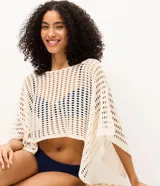 Salida de playa blusa blanca de punto calado, con diseño cropped, cuello bote y mangas largas amplias.
