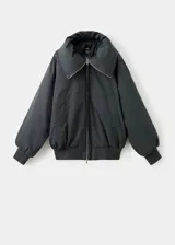Chaqueta estilo bomber color negro, de corte oversize, con cuello alto amplio, cierre frontal de cremallera metálica y bolsillos laterales.