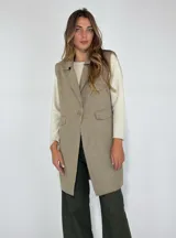 Chaleco largo color beige, con cuello solapa, un botón frontal y dos bolsillos de parche. Presenta costuras decorativas en contraste.