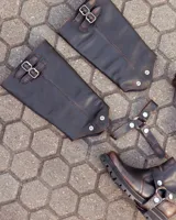 Bota de caña alta confeccionada en cuero color marrón caoba con acabado desgastado. Presenta una suela track robusta, correas con hebillas en la parte superior de la caña y un arnés decorativo con herrajes metálicos en el tobillo.