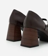 Zapato estilo Mary Jane de poliuretano color marrón oscuro, con punta redondeada, tira con hebilla ajustable sobre el empeine y taco bloque de altura media con acabado símil madera.