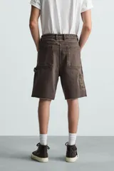 Bermuda relaxed fit confeccionada en tejido de algodón con efecto lavado. Presenta un diseño de cinco bolsillos, bolsillo multifunción en la pernera y tira lateral de estilo carpintero. Cuenta con cierre frontal con cremallera y botón.