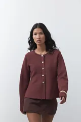 Cardigan negro de tejido de punto con cuello redondo y cierre frontal con botones a contraste. Presenta un corte entallado en la cintura con una silueta levemente evasé y mangas largas.