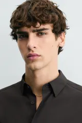 Camisa de corte slim fit, color negro, con cuello italiano, manga larga con puños abotonados y cierre frontal de botones. Confeccionada en tejido de fácil cuidado que minimiza la necesidad de planchado.