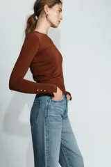 Jersey de punto liso color negro, con cuello redondo y manga larga. Presenta una hilera de cuatro botones dorados decorativos en el puño de cada manga.