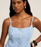 Chaleco largo de jean con escote recto, breteles finos ajustables y cierre frontal con botones. Presenta un corte acinturado con pences, bolsillos delanteros decorativos y ruedo en punta.