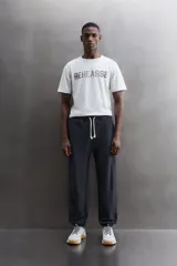 Camiseta de algodón gris melange con cuello redondo, mangas cortas y efecto lavado. Presenta un estampado de texto frontal en color oscuro con efecto desgastado.