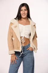 Campera tipo gamulán de gamuza color tostado con interior y solapas de corderito sintético color crema. Presenta cierre frontal con botones, bolsillos cuadrados delanteros y detalles de costuras visibles.