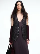 Chaleco sastrero de denim negro con diseño de cuadros y aplicación de lentejuelas sutiles. Presenta escote en V, cierre frontal con botones metálicos y bolsillos delanteros.