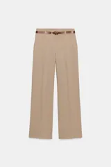Pantalón de vestir color beige, tiro alto, corte ancho y pierna recta. Presenta un bajo con vuelta y viene acompañado de un cinturón fino de cuero marrón con hebilla metálica.