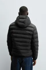 Campera puffer acolchada de corte regular fit en color negro, confeccionada en tejido técnico repelente al agua. Presenta cuello subido con capucha, cierre frontal de cremallera, mangas largas con puños elásticos y bolsillos laterales de vivo.