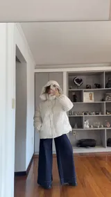 Campera puffer de corte holgado en color beige, con diseño acolchado, cuello alto y capucha desmontable. Cuenta con cierre frontal y botones a presión, además de puños elásticos.