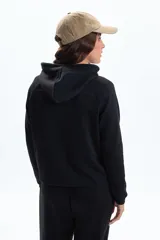 Campera deportiva negra con cierre frontal, capucha con cordones y bolsillos canguro. Presenta un corte ligeramente corto y mangas raglán.