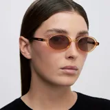 Lentes de sol con montura ovalada de color amarillo traslúcido y lentes color marrón. Diseño de bordes finos con protección UV400 y lentes polarizadas.