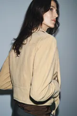 Chaqueta estilo biker de piel de ante 100% color beige, con cuello solapa, manga larga, bolsillos con cremalleras metálicas y bajo ajustable con hebilla. Cierre frontal con cremallera metálica.