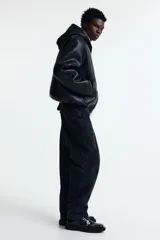 Pantalón estilo carpenter de corte holgado, confeccionado en tejido de algodón. Presenta tiro caído, bolsillos laterales de parche, trabilla funcional en una pierna y costuras reforzadas visibles sobre y debajo de las rodillas.