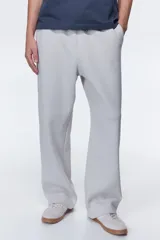 Pantalón deportivo en felpa pesada de mezcla de algodón, color gris claro, de corte holgado con cintura elástica ajustable mediante cordón y bolsillos laterales.