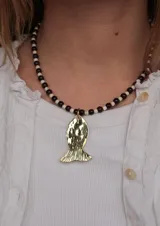 Collar corto con cuentas esféricas marrones y blancas intercaladas, con un dije central dorado en forma de pez con textura martillada.