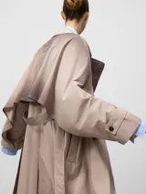 Gabardina cruzada color beige con efecto envejecido, de corte recto y largo midi. Presenta doble solapa en el lado derecho, doble botonadura frontal, bolsillos laterales, mangas largas con trabillas en los puños y canesú amplio en la espalda.