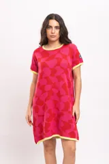 Vestido corto tejido de punto con diseño geométrico abstracto en tonos rojo y fucsia, cuello redondo, mangas cortas y bolsillos laterales, con detalles en amarillo en el cuello, puños y ruedo.
