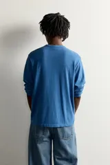 Camiseta de manga larga color azul con cuello redondo, corte relajado y pequeño parche gráfico bordado en el pecho.