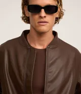 Campera estilo bomber de poliuretano (PU) símil cuero en color negro, con cuello, puños y dobladillo acanalados, y cierre frontal de cremallera.